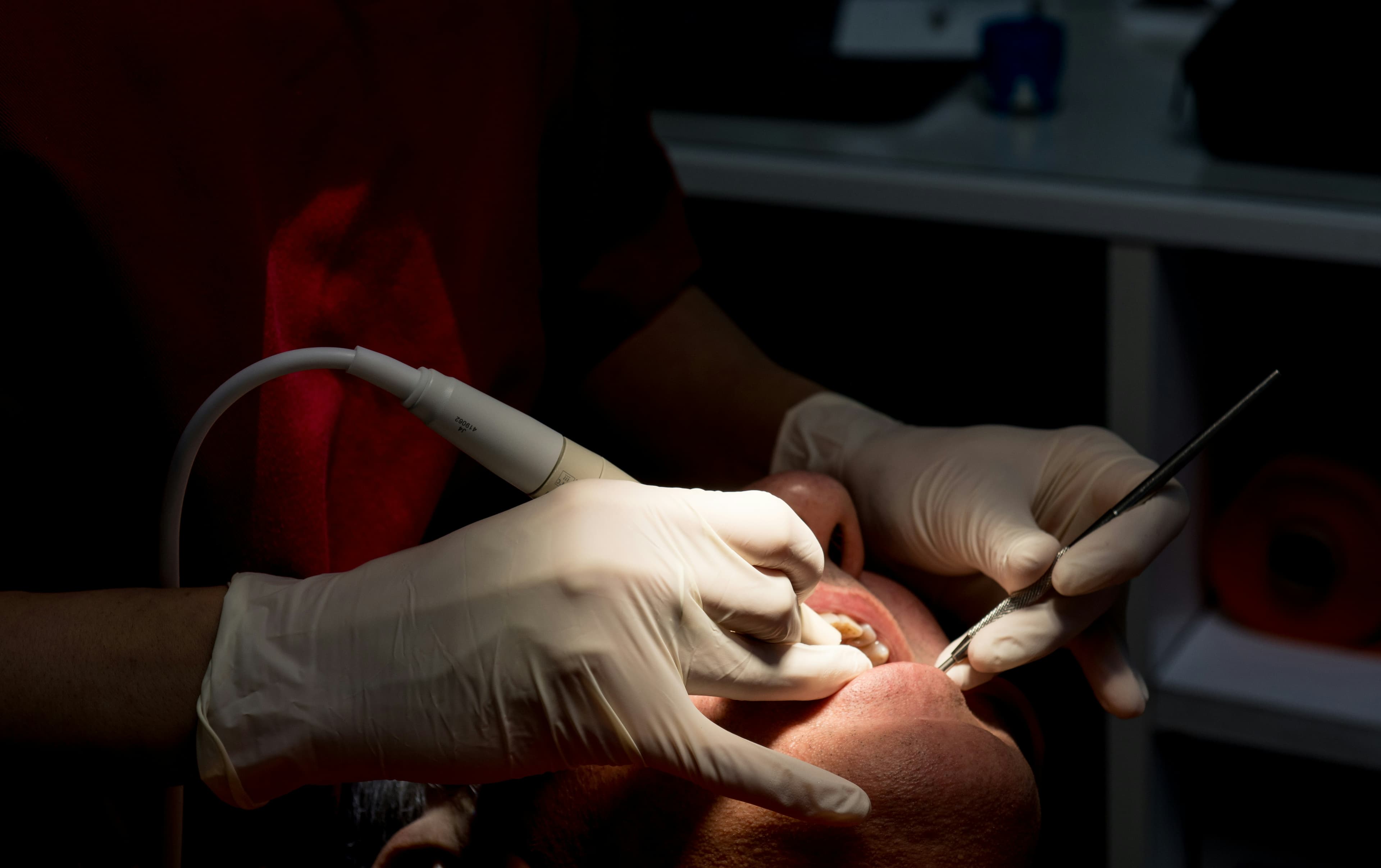 A dentist cleaning a patient's teeth with dental scaling tools